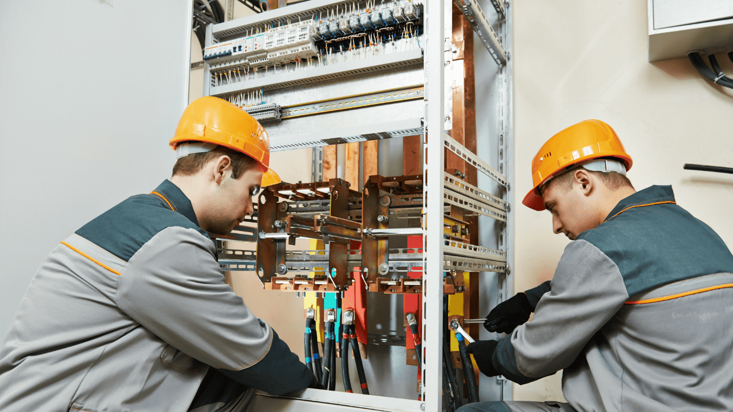 Two electricians work on a large commercial electrical system.