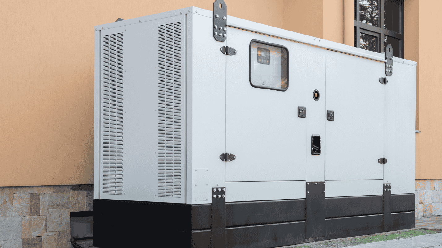 A large backup generator sits outside of the walls of a commercial building.