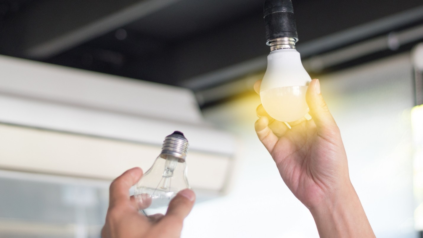 A person screws in an LED bulb after removing an old lightbulb.