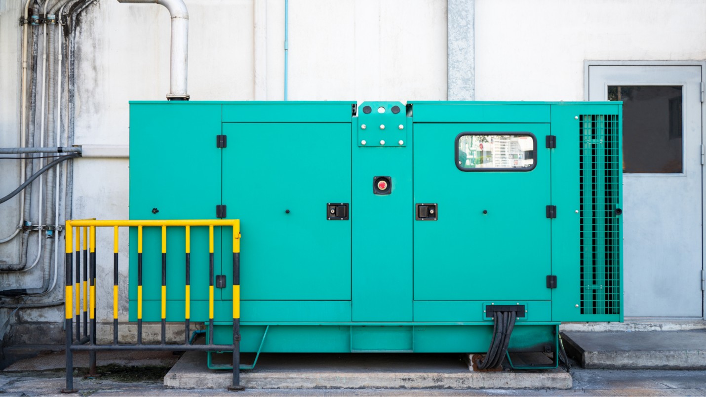 A large teal colored backup generator attached to a commercial building.